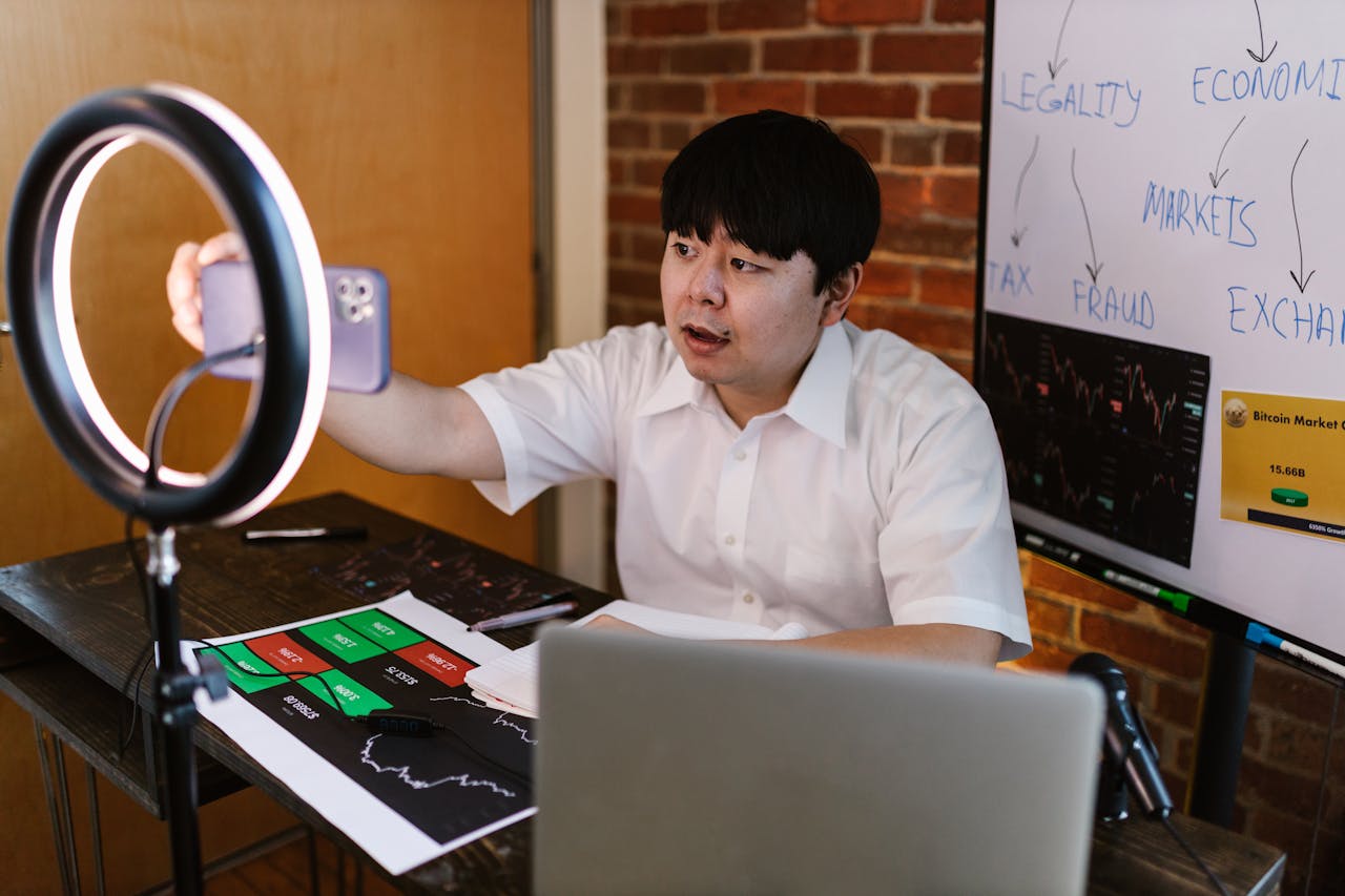 Young man filming a vlogger video about cryptocurrency trading with charts and graphs.